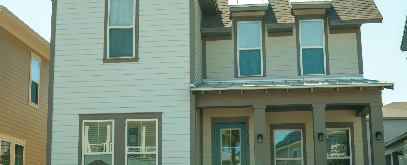Two-story modern suburban house with a front porch, large windows, and neatly trimmed lawn on a sunny day