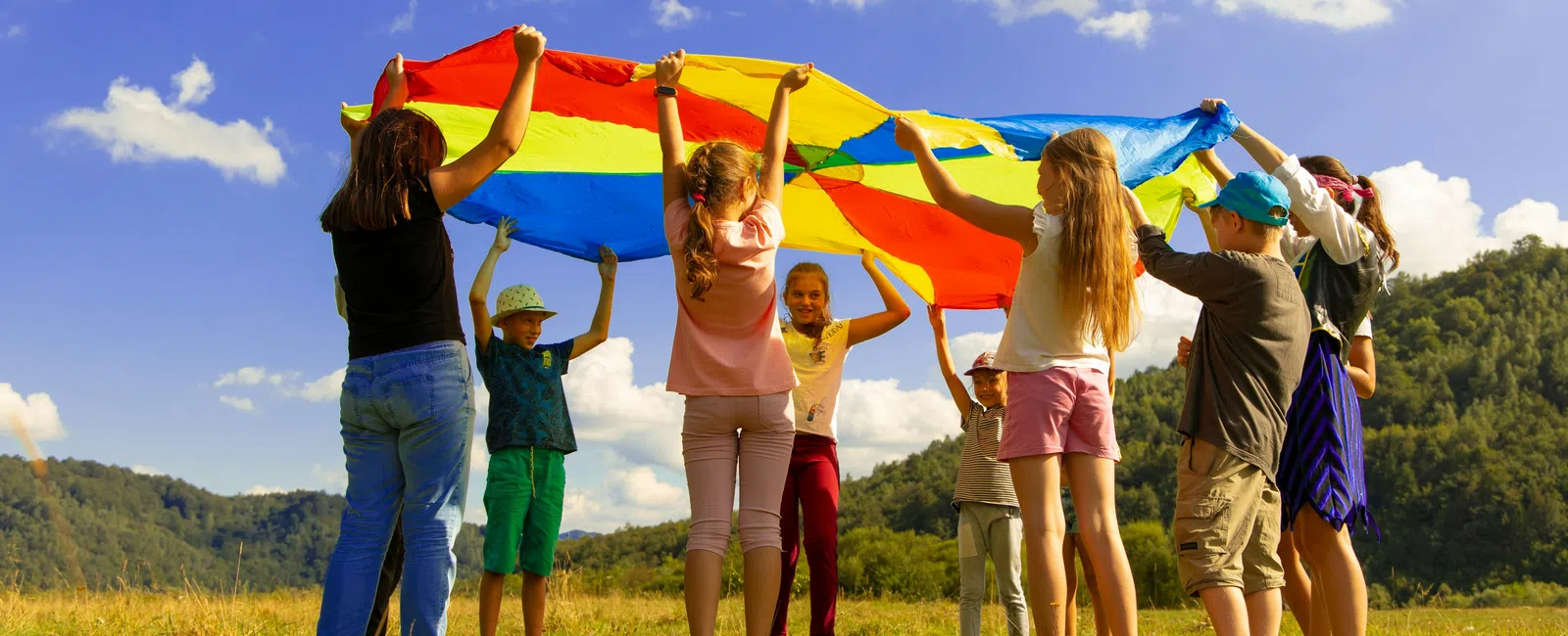 Group of children playing with a colorful parachute outdoors on a sunny day in a grassy field.