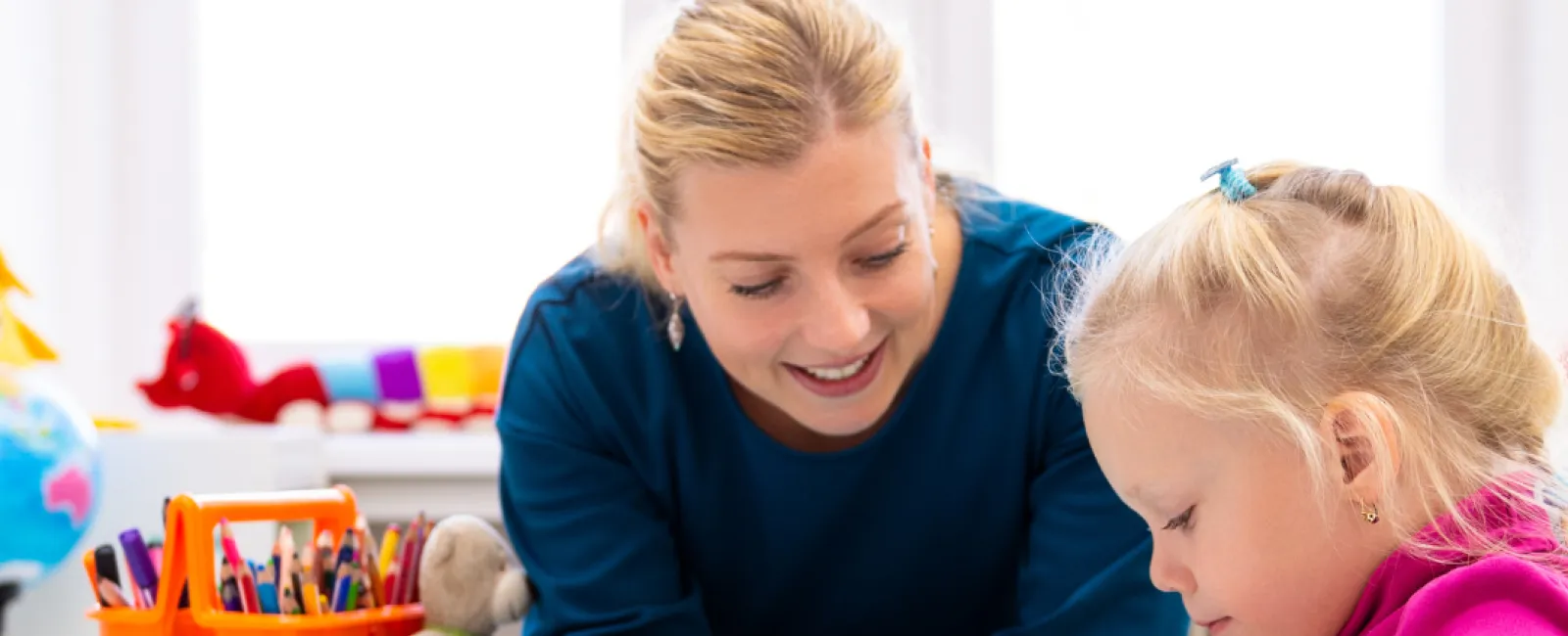 Teacher engaging with young girl doing arts and crafts with colorful modeling clay at a table