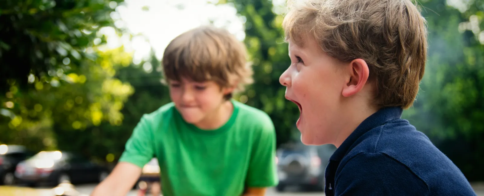 Two young boys playing and laughing outdoors near a pink inflatable pool on a sunny day.