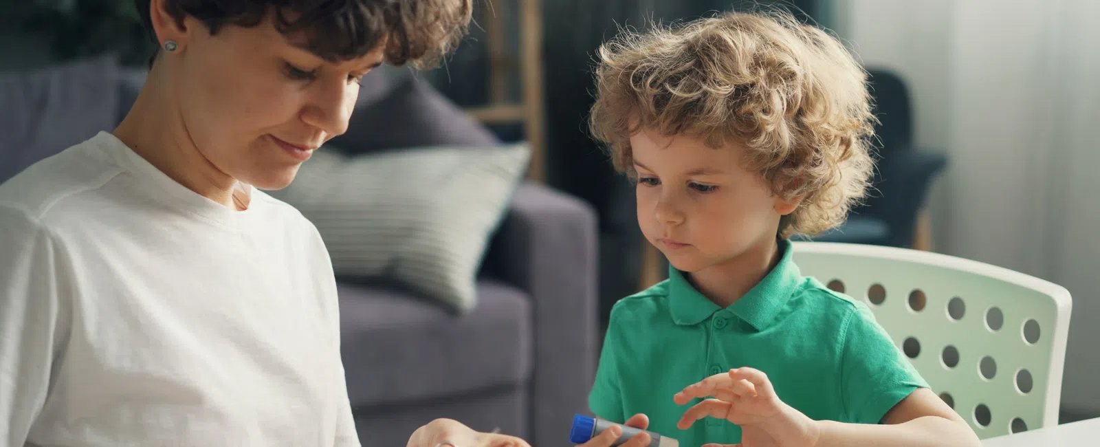Adult and child crafting together using scissors and glue at a table with paper pieces in a cozy room.