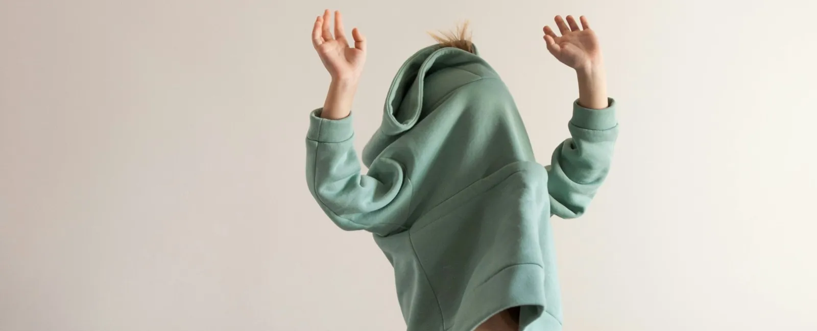 Child in green hoodie lifting their top over their head playfully in a cozy living room.