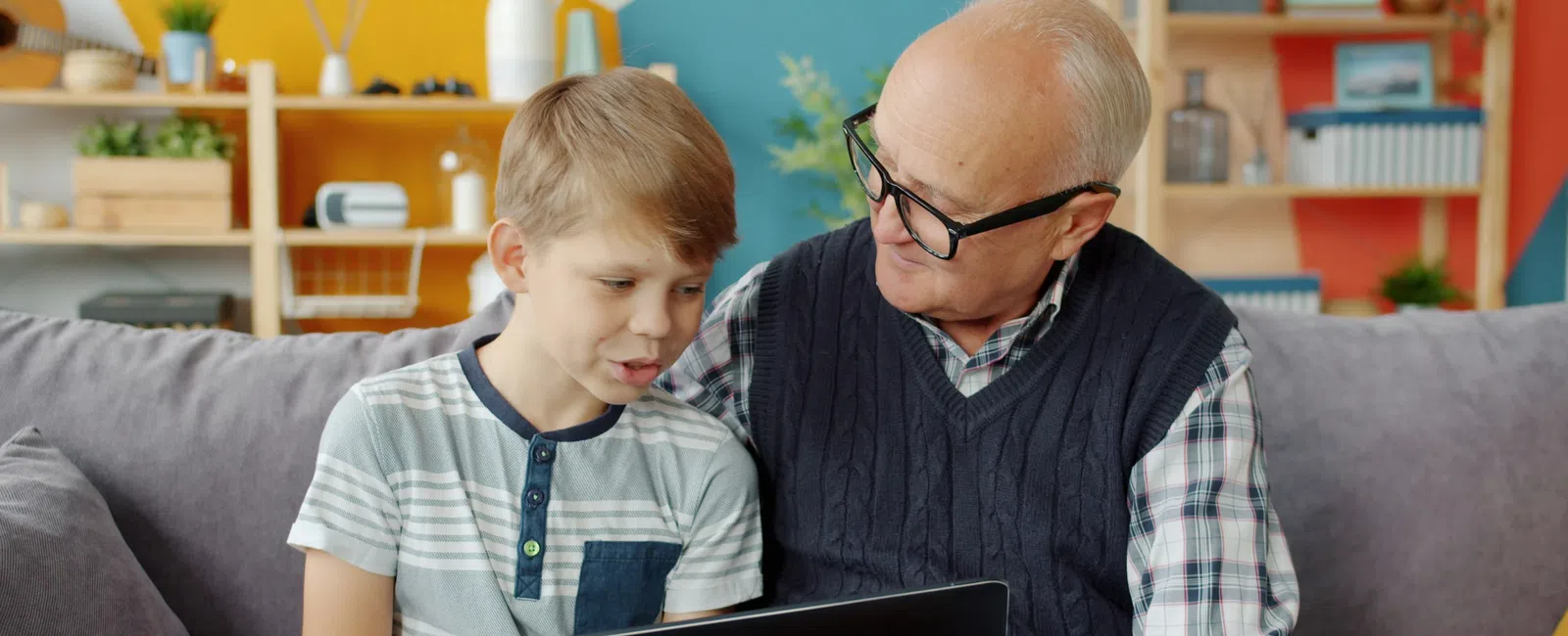 Grandfather and grandson sitting on a couch using a tablet together in a colorful living room.