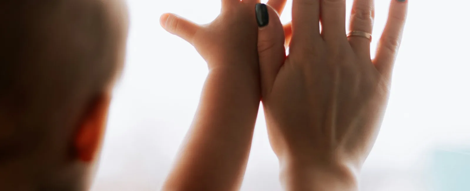 Child and adult hands touching a window, illustrating connection and growth with soft natural light.