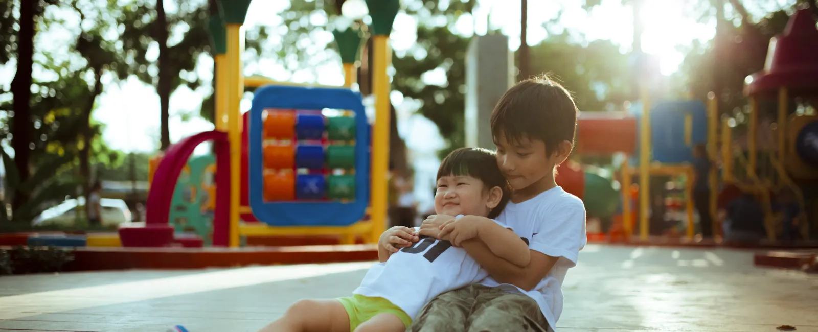Two children playing and hugging at a colorful playground with softened sunlight in the backgrounda
