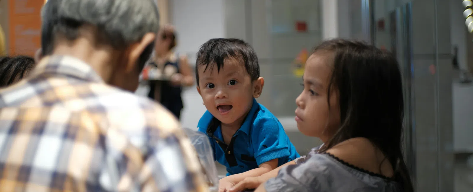 Young children interacting with an elderly man at a table in a bright indoor setting.