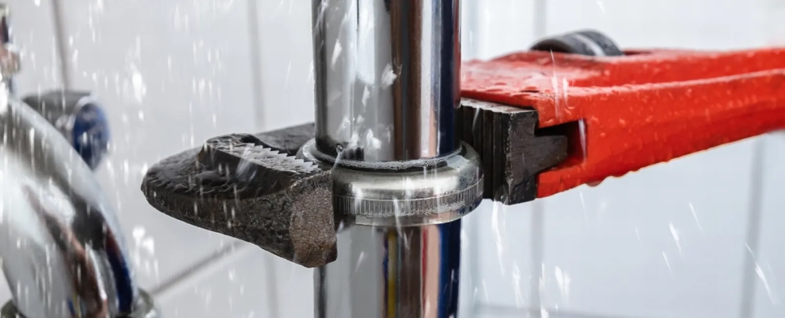 Close-up of a plumber's wrench tightening a metal pipe with water spraying from a leak.