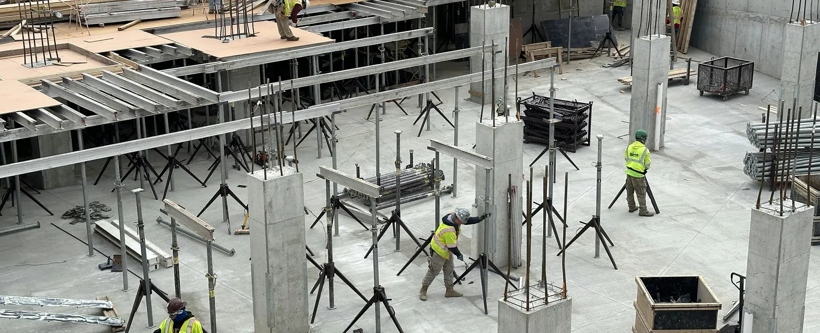 Construction workers in safety gear assembling concrete pillars and scaffolding on a building site