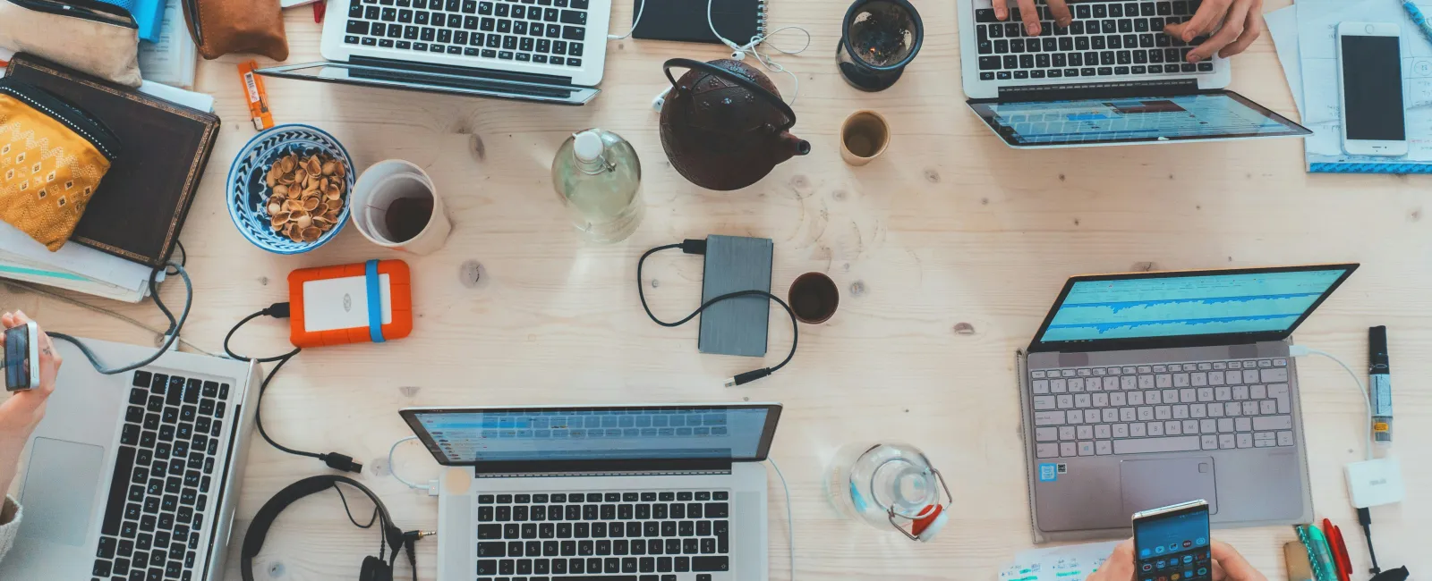Overhead view of a collaborative workspace with laptops, notebooks, coffee, and people working together.