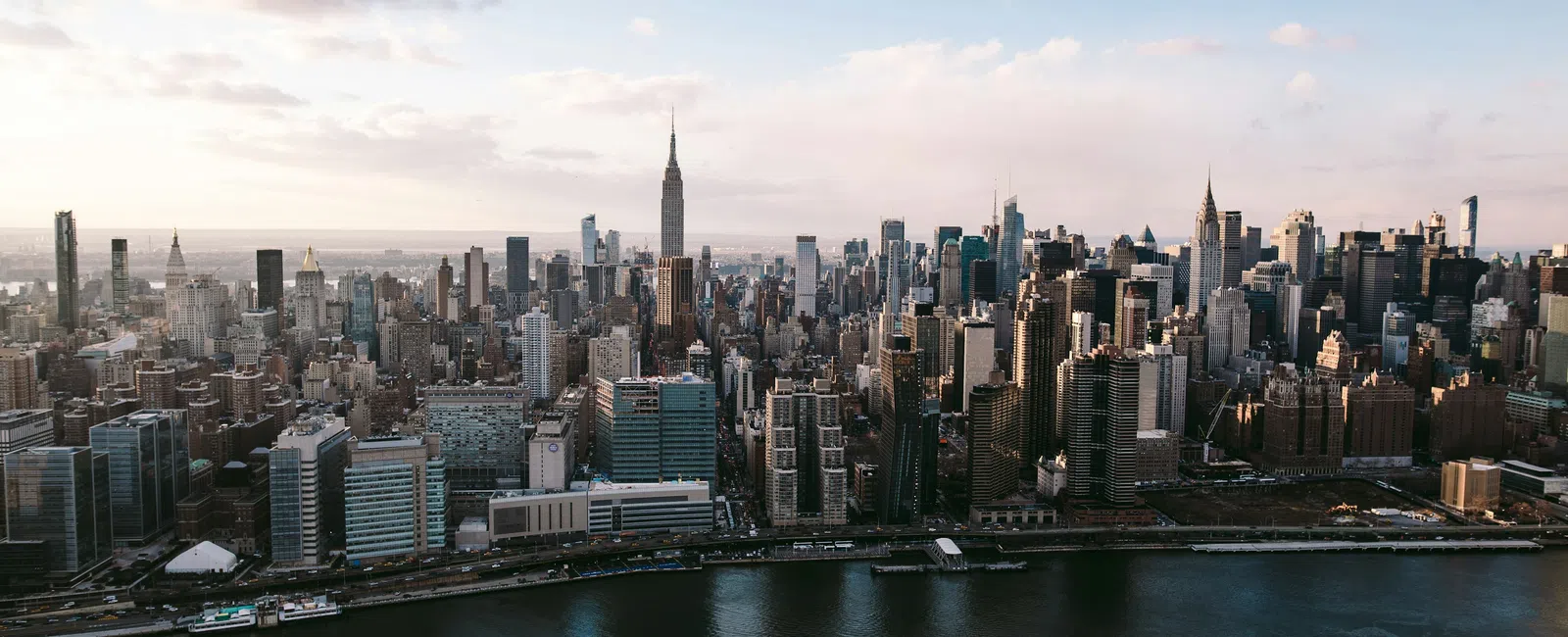 Aerial view of Manhattan skyline with Empire State Building and Hudson River under a partly cloudy sky.