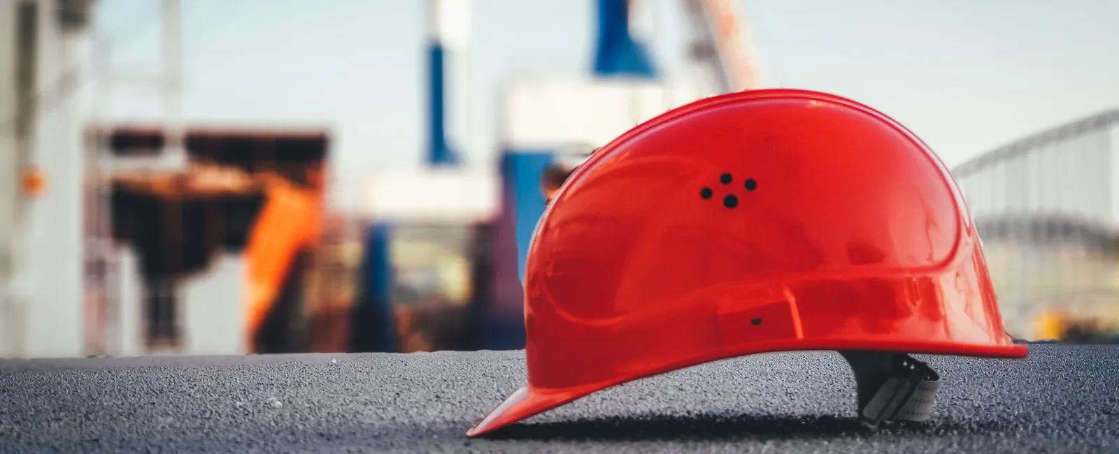 Red construction safety helmet on textured surface with blurred construction site background and workers.