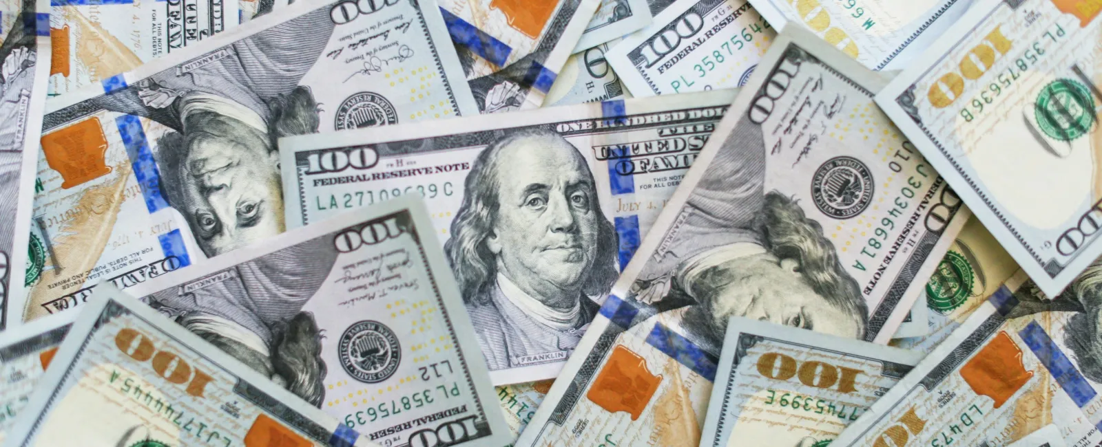 Pile of US hundred-dollar bills with Benjamin Franklin's portrait and security features visible