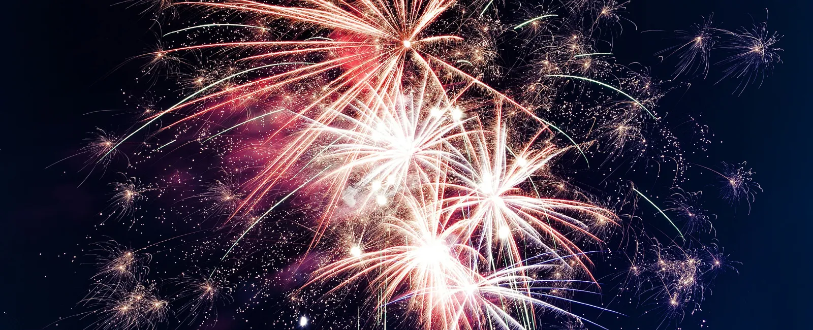 Bright white and red fireworks exploding against a dark night sky during a celebration event.
