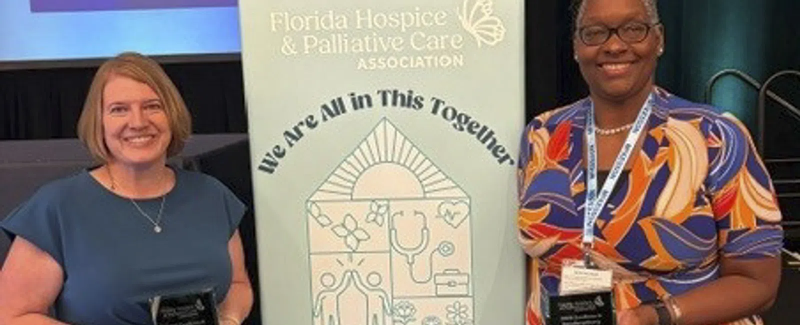 Two women holding awards next to a sign for the Florida Hospice & Palliative Care Association Annual Forum
