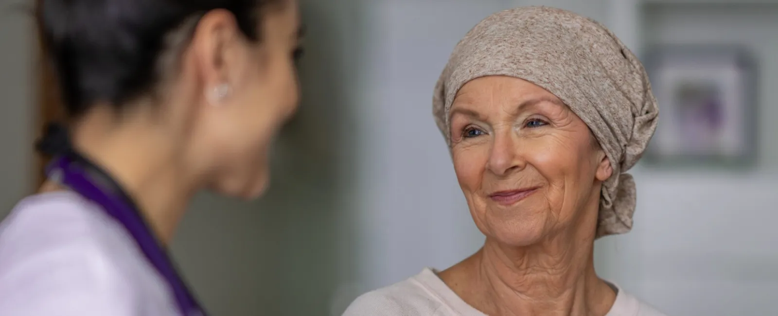 Smiling elderly woman wearing a headscarf talks with a healthcare professional in a caring consultation.