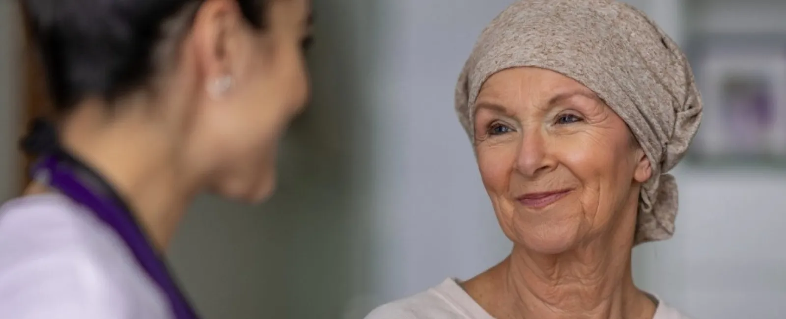 Smiling elderly woman wearing a headscarf talking with a female healthcare professional in a medical setting
