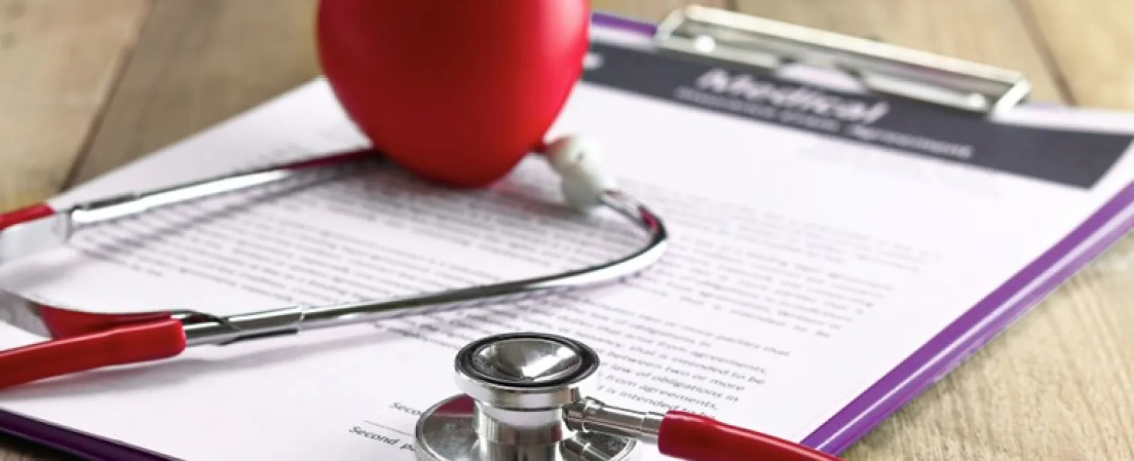 Red stethoscope and heart model on medical documents on a wooden desk representing healthcare.