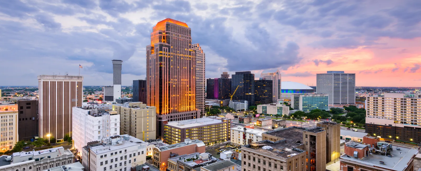 City skyline at sunset with illuminated tall buildings under dramatic cloud-covered sky.