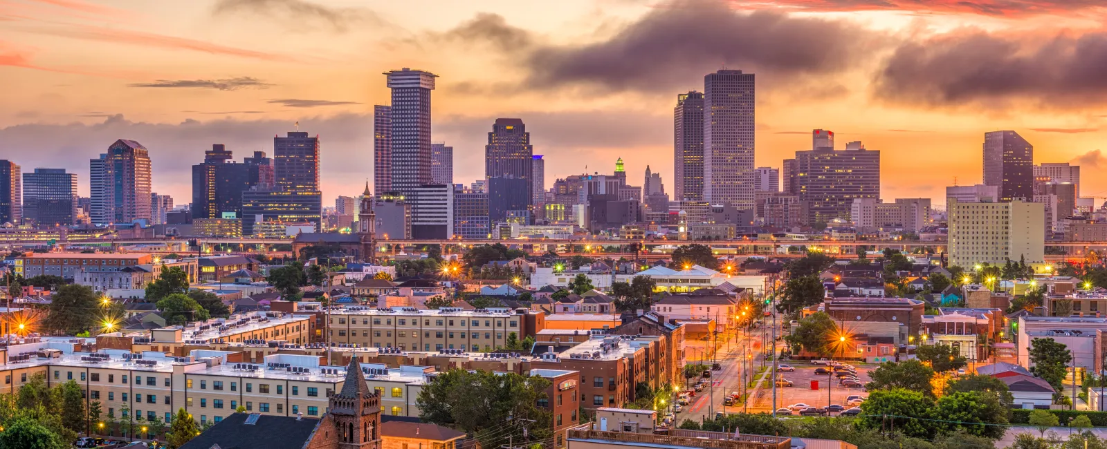 New Orleans city skyline at sunset with colorful sky and illuminated buildings in vibrant urban setting.