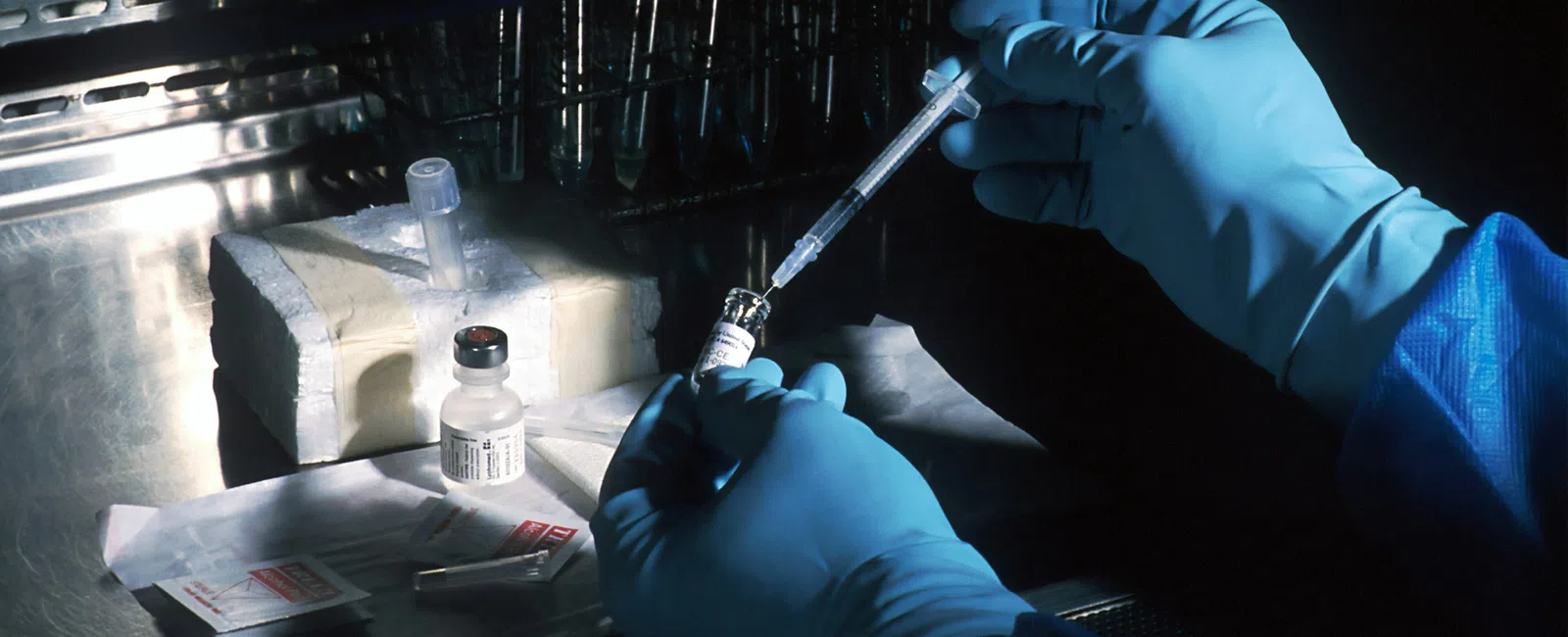 Scientist wearing blue gloves preparing a vaccine syringe in a laboratory with test tubes and medical supplies