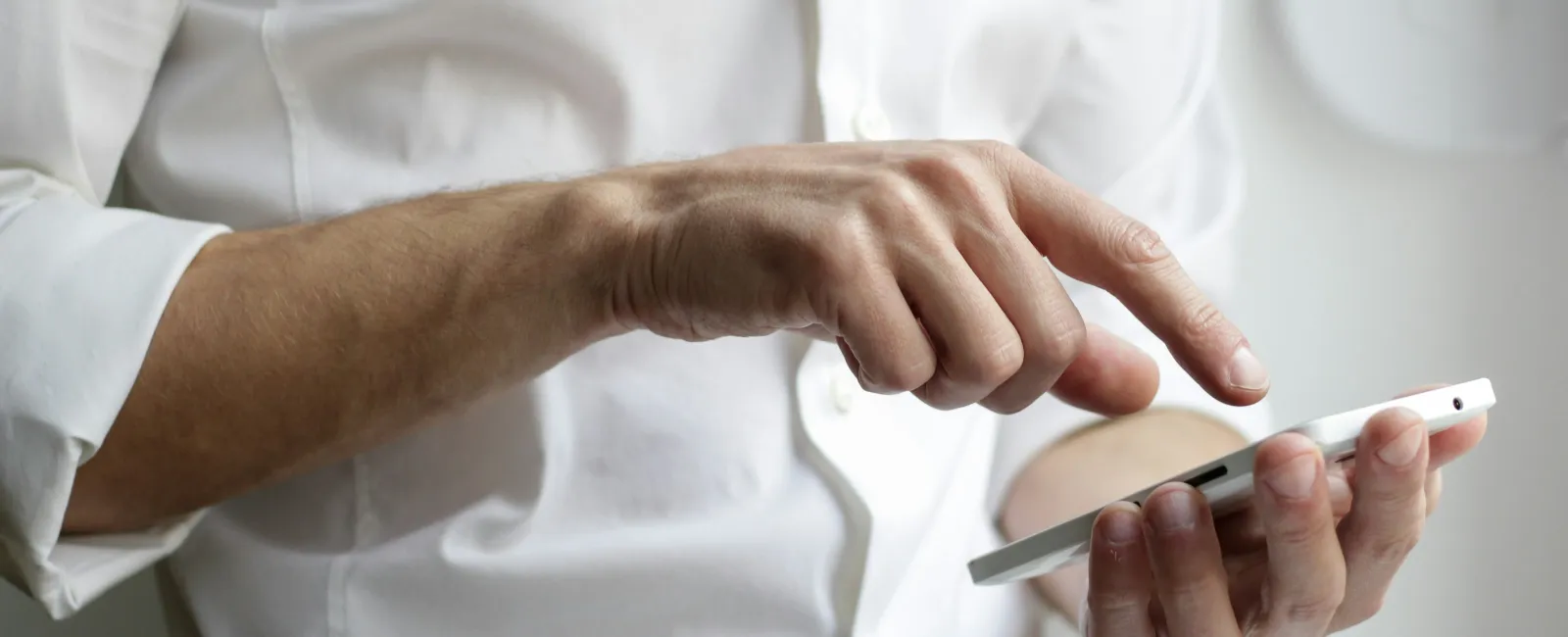 Man in white shirt using a smartphone with one hand while tapping the screen with the other finger indoors.