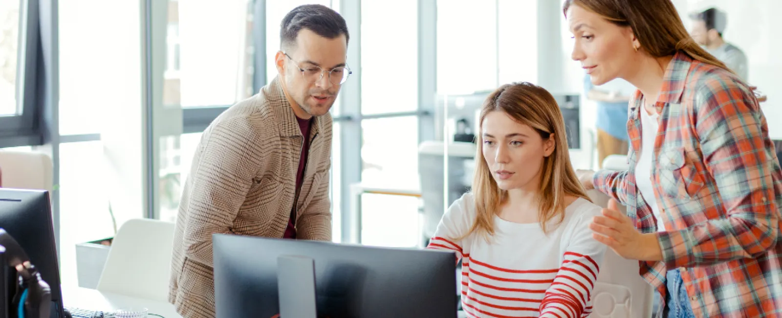 Three colleagues collaborating and discussing work while looking at a computer screen in a modern office.