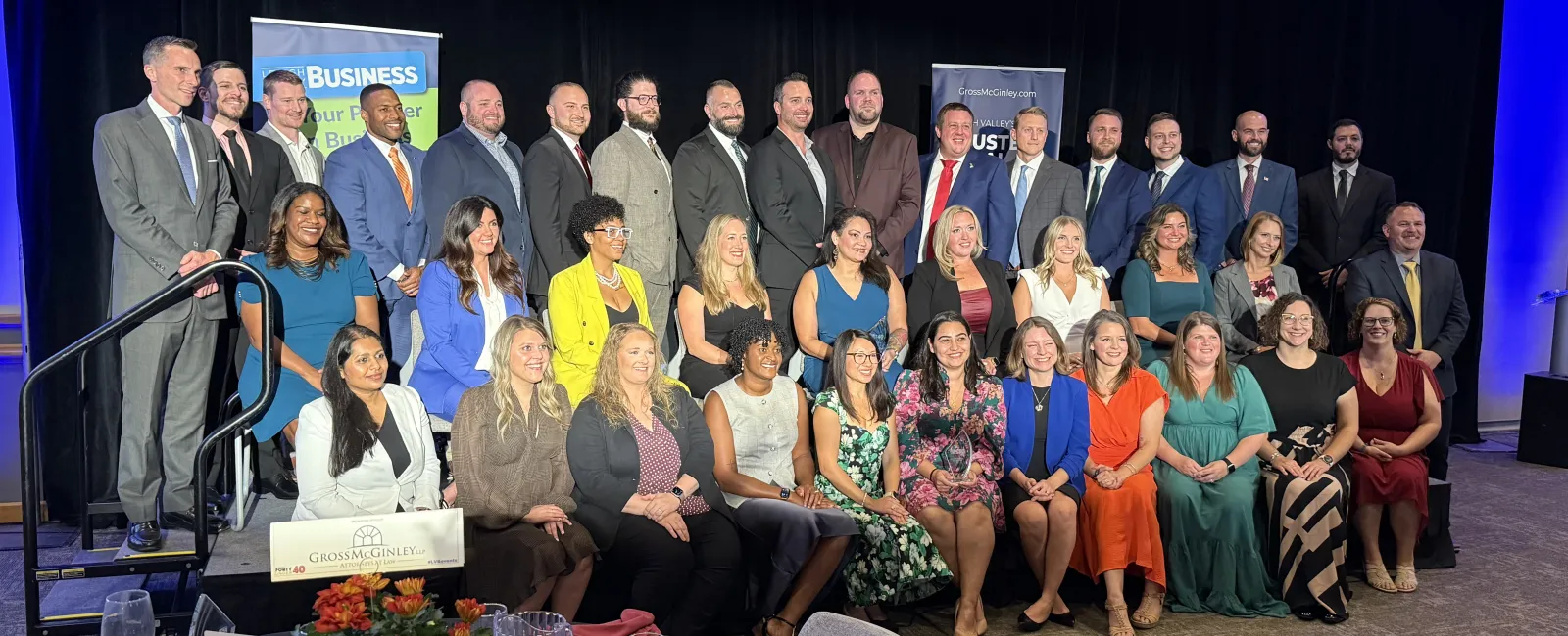 Group photo of diverse professionals at a formal business event with banners in the background