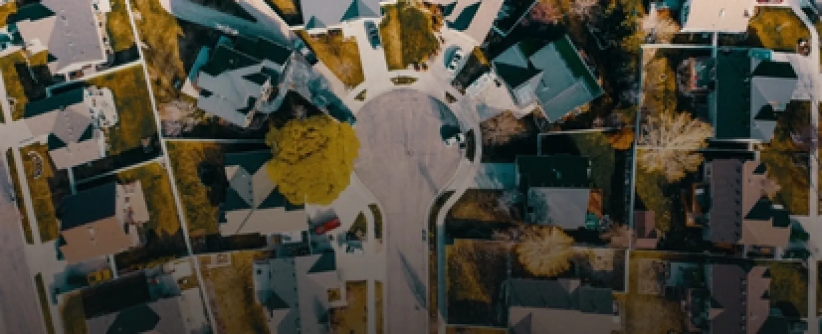 Aerial view of suburban neighborhood with houses around a roundabout street and autumn trees.