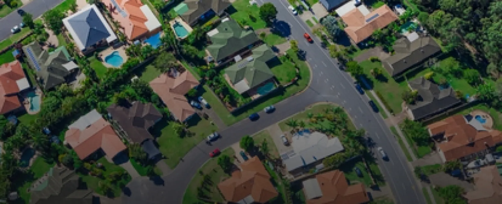 Aerial view of a suburban neighborhood with houses, green lawns, swimming pools, and winding roads.