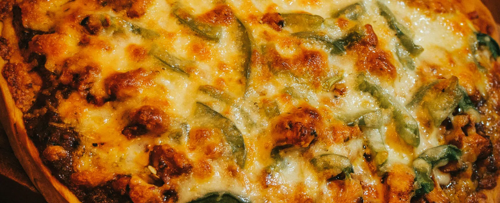 Close-up of a freshly baked pizza topped with melted cheese and green bell peppers on a wooden board.