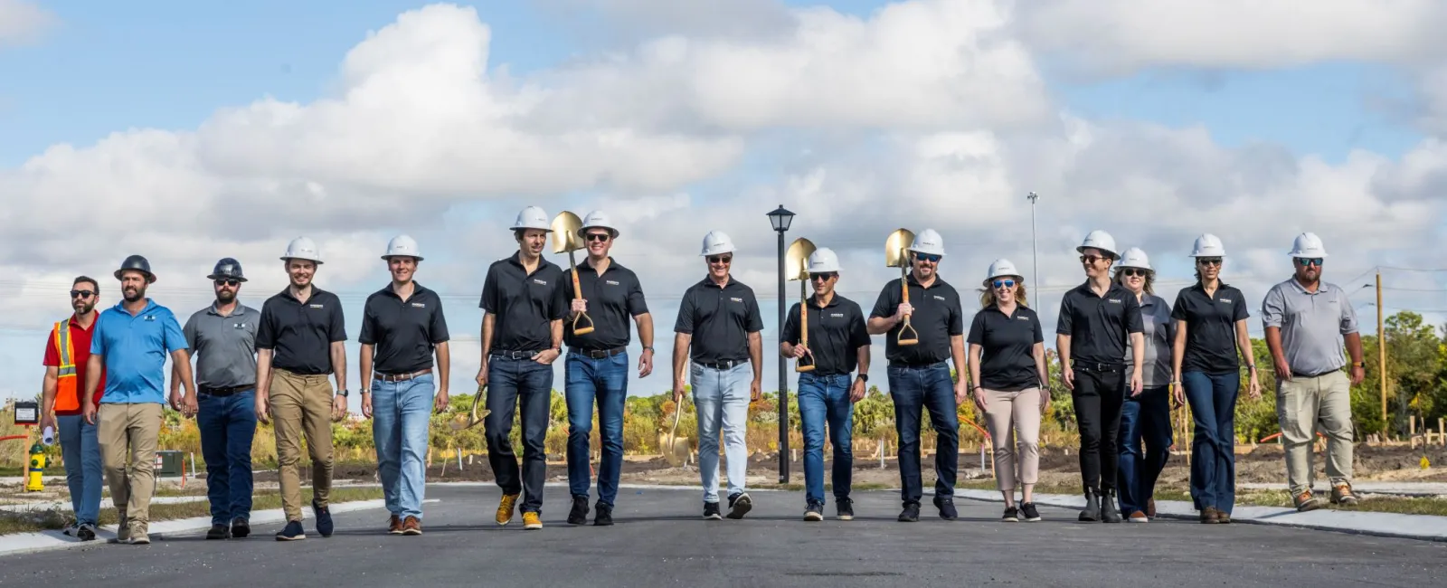 Group of construction workers wearing helmets walking on site under blue sky with clouds