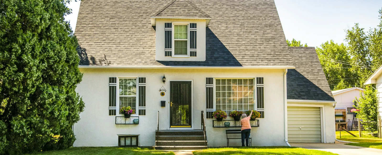 Person arranging flowers in window boxes of a white suburban house with black shutters on a sunny day