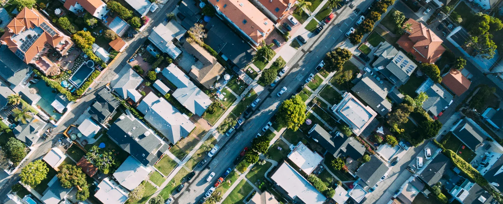 Aerial view of a residential neighborhood with houses, streets, trees, and cars during daytime.
