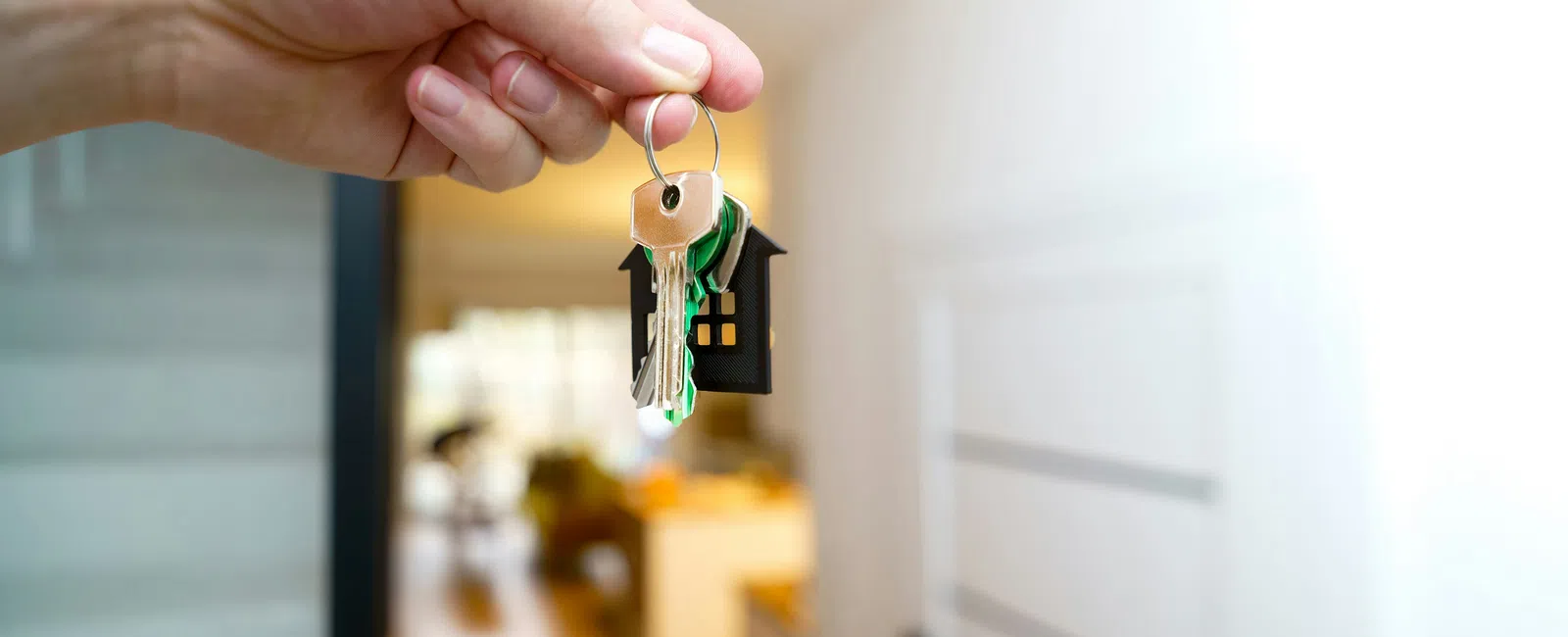 Hand holding house-shaped keychain with keys indoors near a white door and blurred background