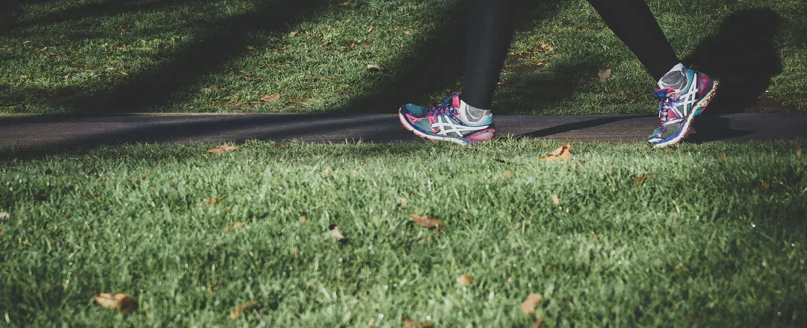 Person walking on a paved path wearing colorful running shoes and black leggings in a grassy park area.