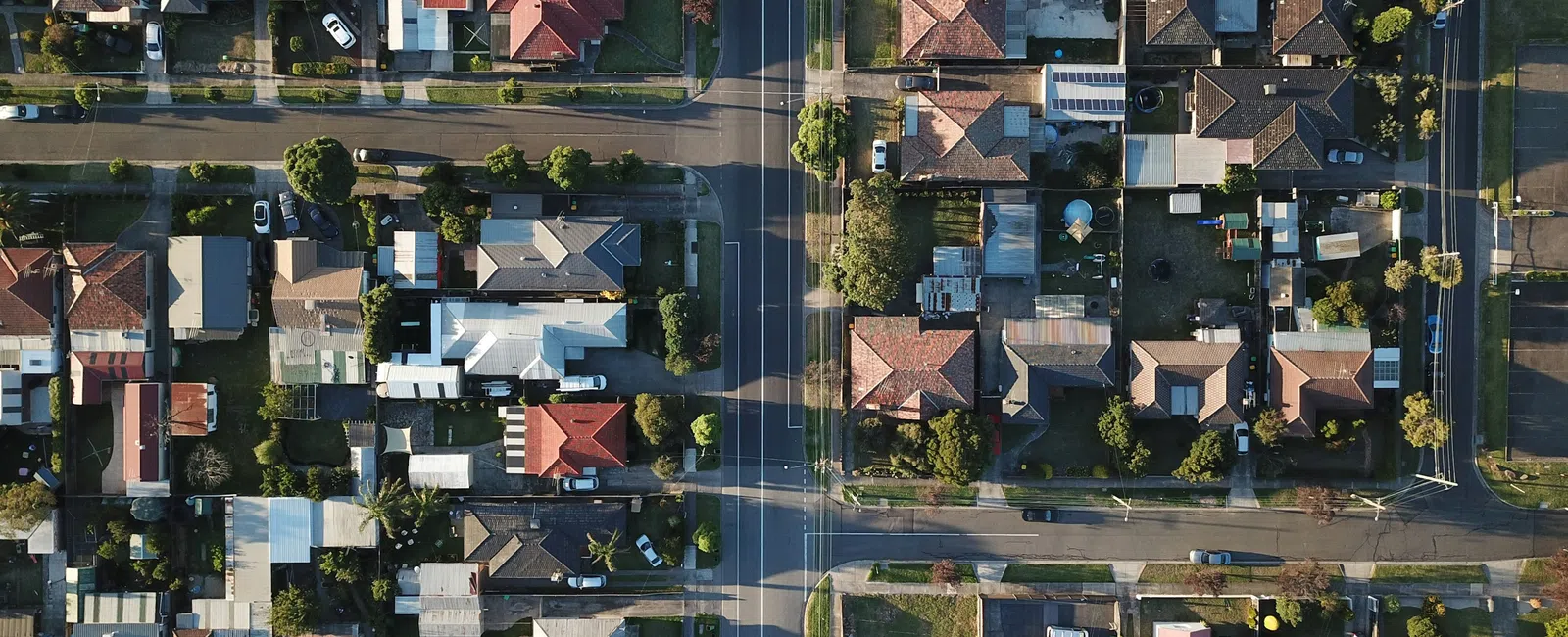 Aerial view of a suburban neighborhood showing houses, streets, and trees in a grid layout under clear daylight.