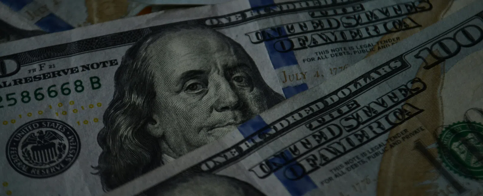 Close-up of multiple United States 100 dollar bills featuring Benjamin Franklin's portrait.