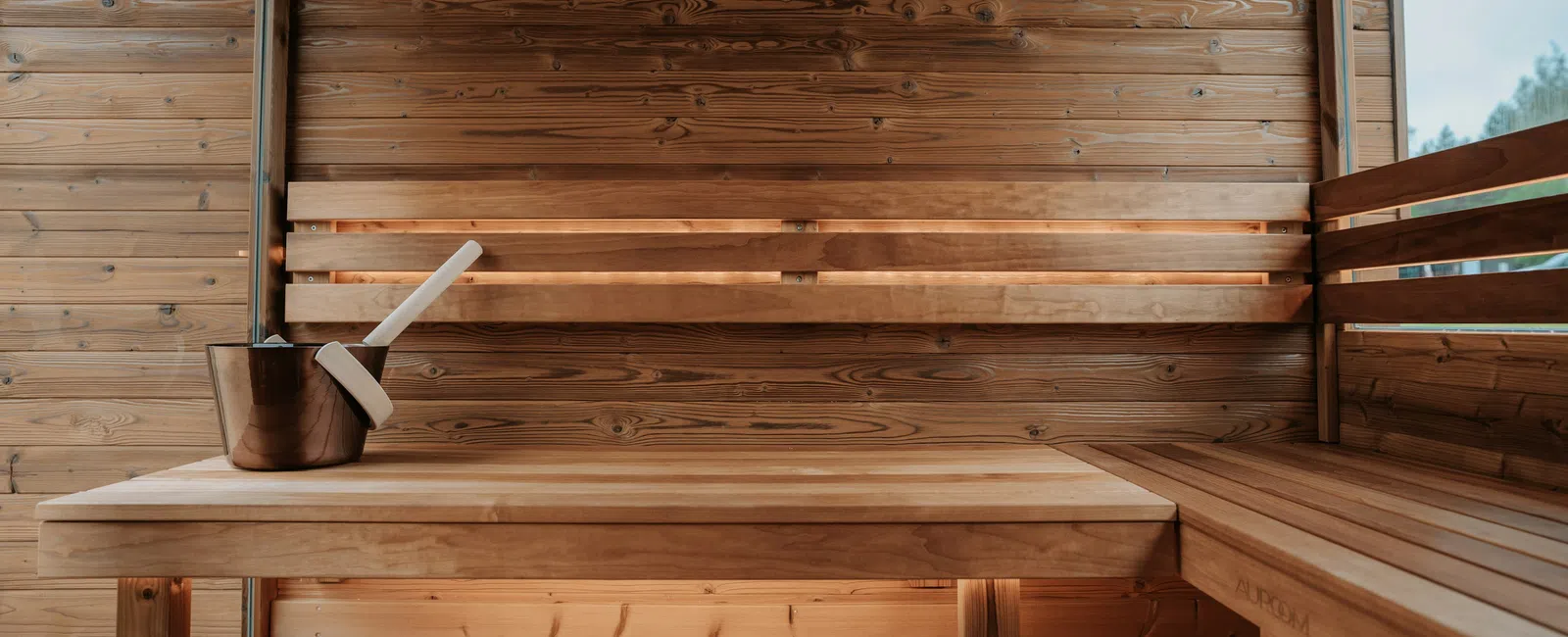 Cozy wooden sauna interior with bench, bucket, ladle, and overlaid sign reading 'AURORA' on wall.