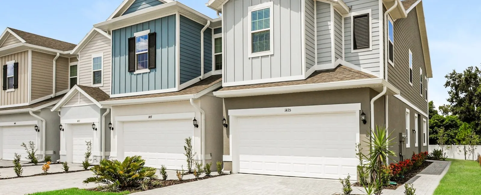 Row of modern townhouses with attached garages, manicured lawns, and bright blue sky on a sunny day.