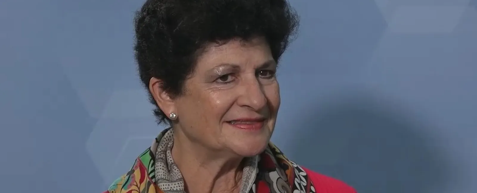 Smiling woman with short curly hair wearing a colorful scarf and red top holding a microphone