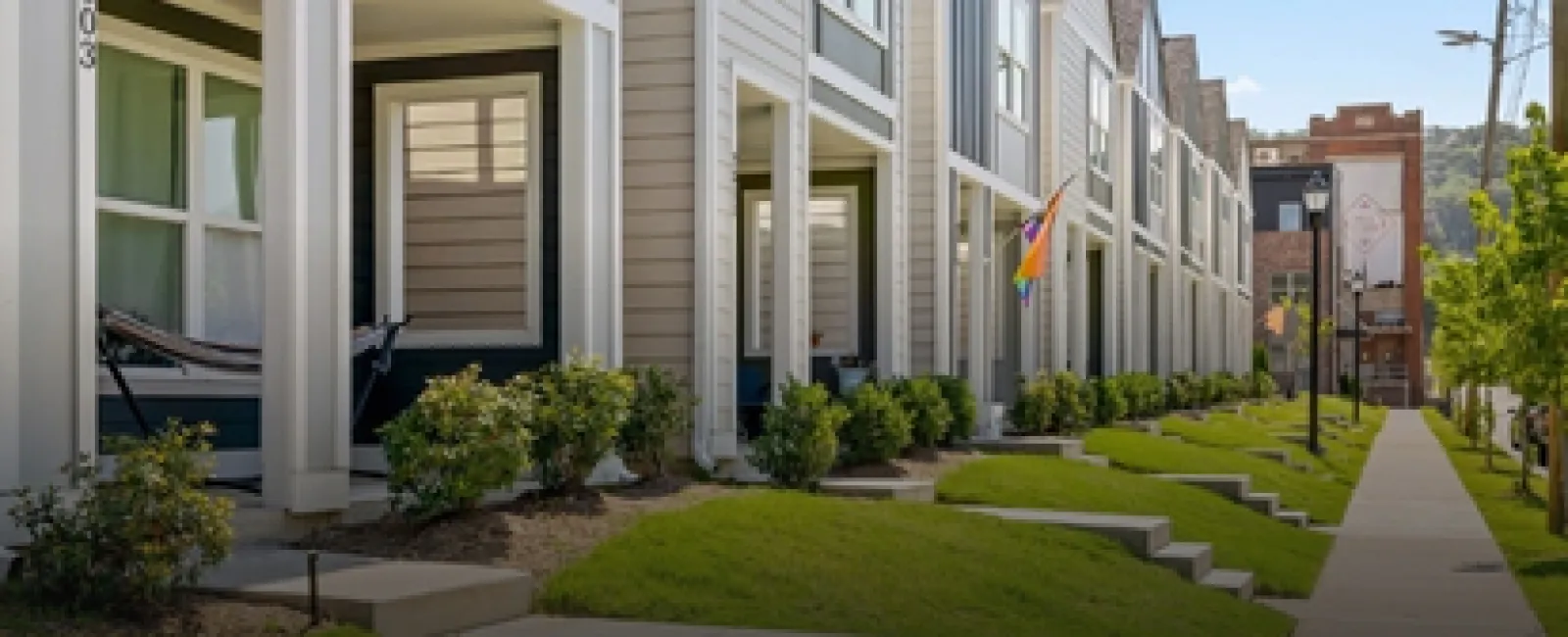 Row of modern townhouses with manicured lawns and a sidewalk under a clear blue sky.