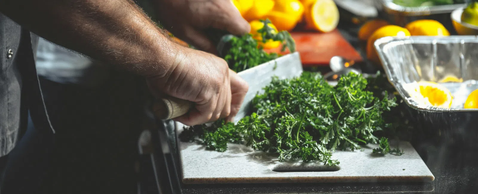 Person chopping fresh parsley on a cutting board in a kitchen with lemons and other ingredients nearby