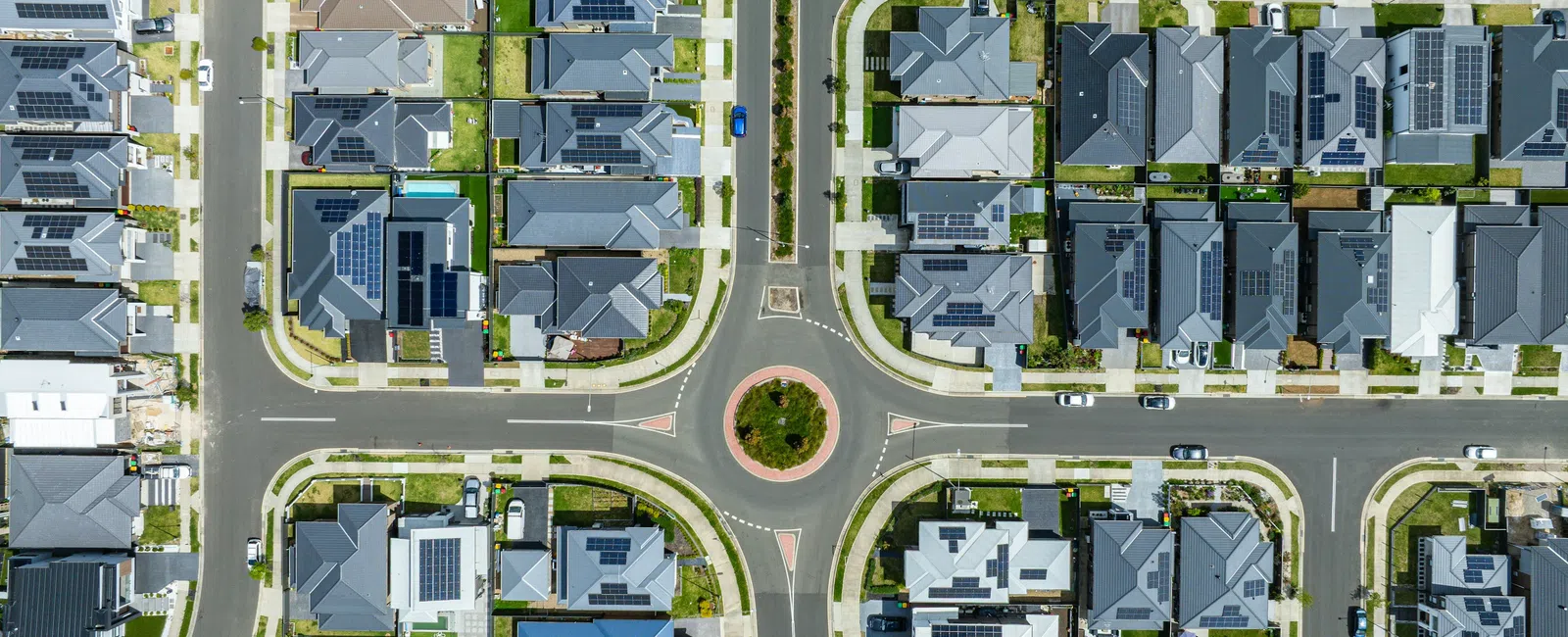 Aerial view of suburban neighborhood featuring a roundabout and houses with solar panels on rooftops.