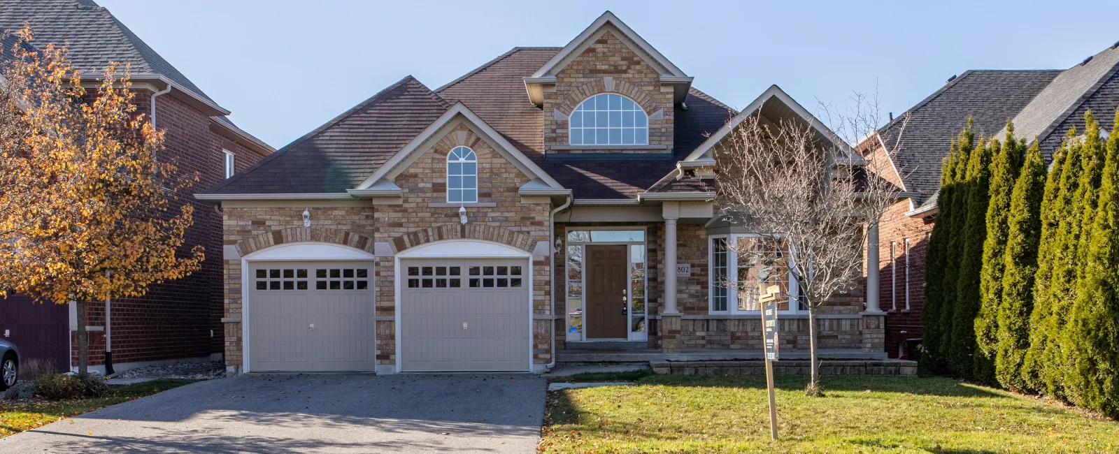 Brick suburban house with two-car garage, arched windows, and a well-maintained front lawn with trees.
