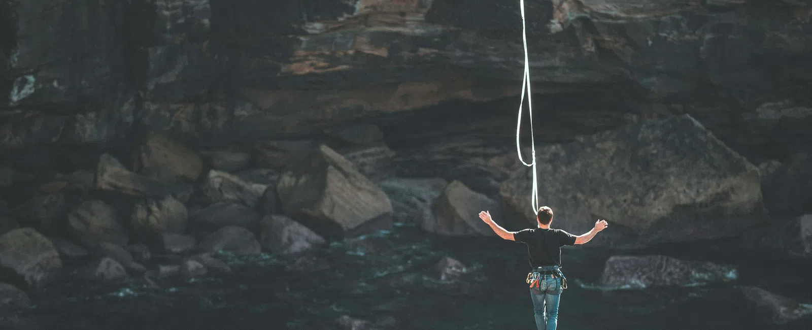 Man balancing on a highline rope against a rocky cliff background, practicing slacklining outdoors.