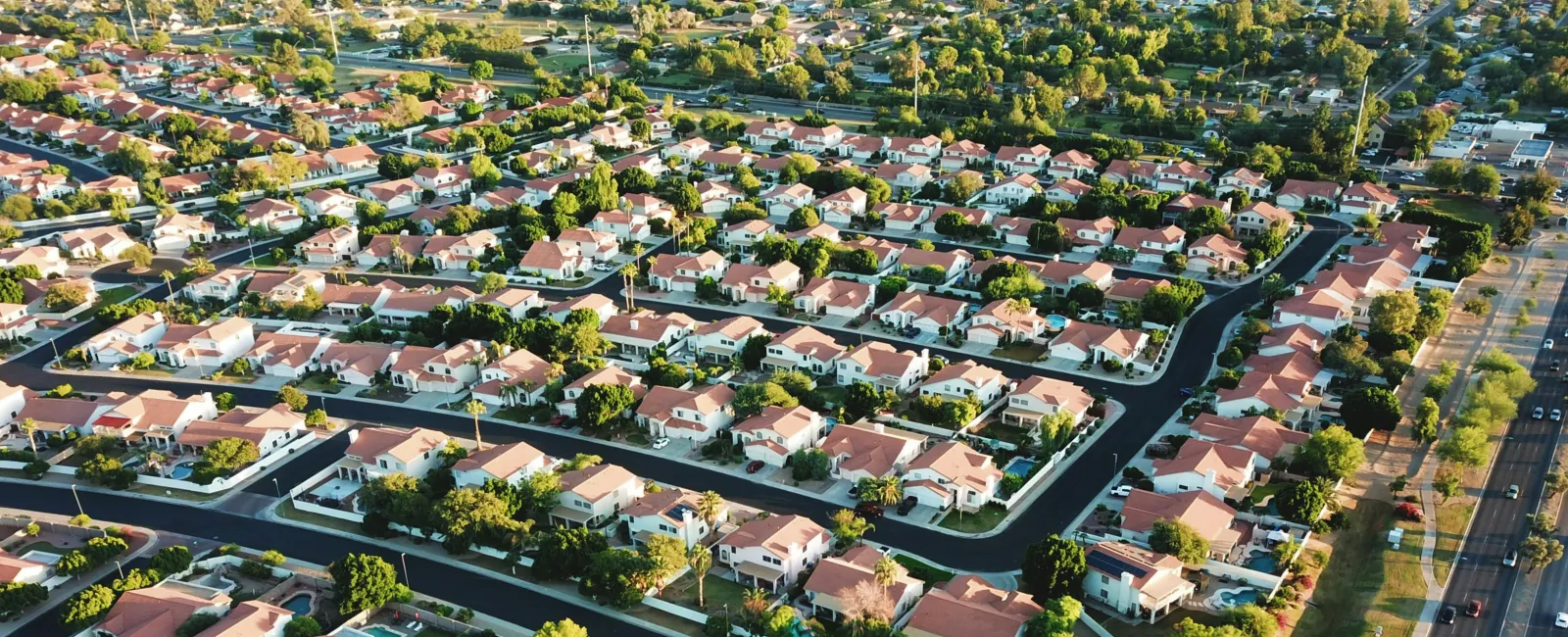 Aerial view of a suburban neighborhood with rows of houses, streets, and greenery under sunlight.