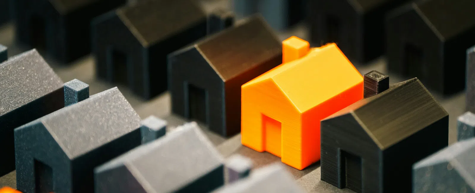 Orange 3D-printed house model stands out among black house models on a grid surface.