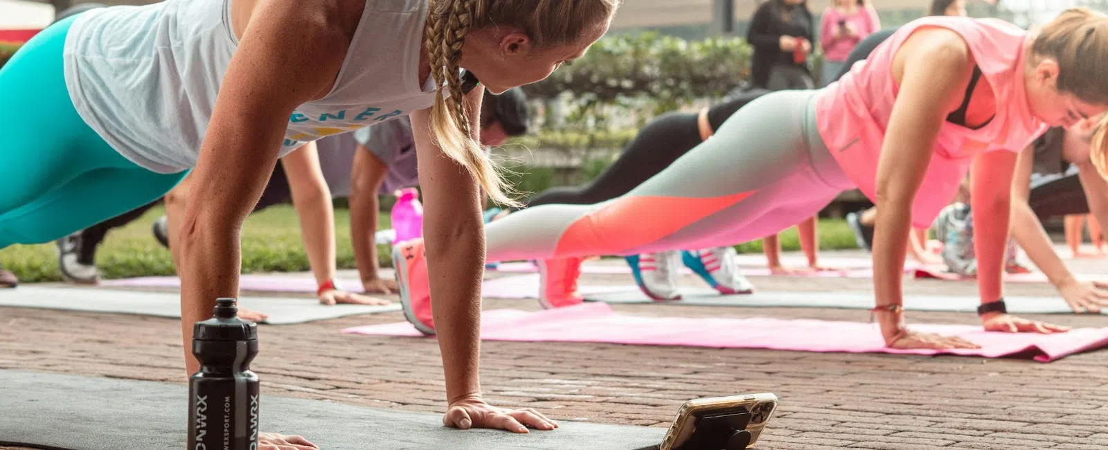 Group of women doing outdoor plank exercise on mats in urban environment with buildings in background