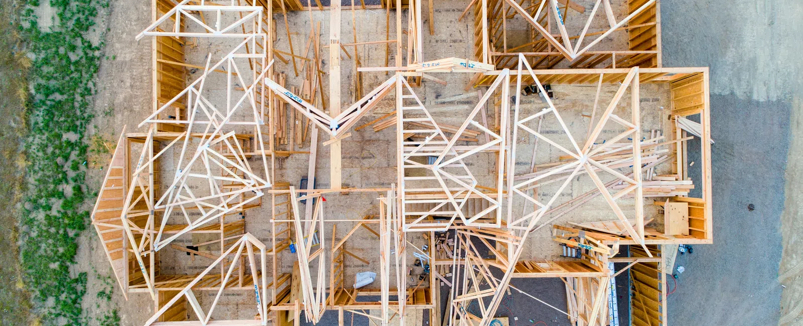 Aerial view of a wooden house frame under construction with visible beams and trusses on a concrete foundation.