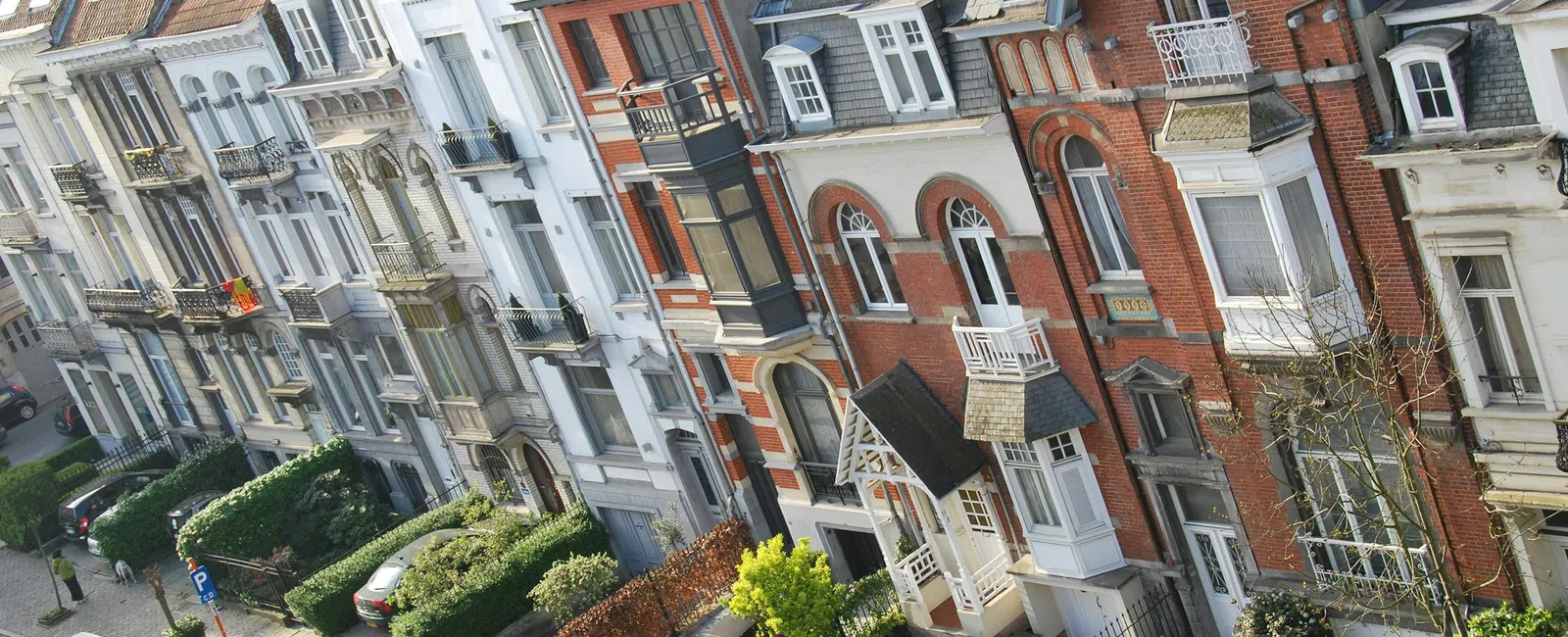 Row of colorful European-style residential buildings with parked cars and greenery along the street.